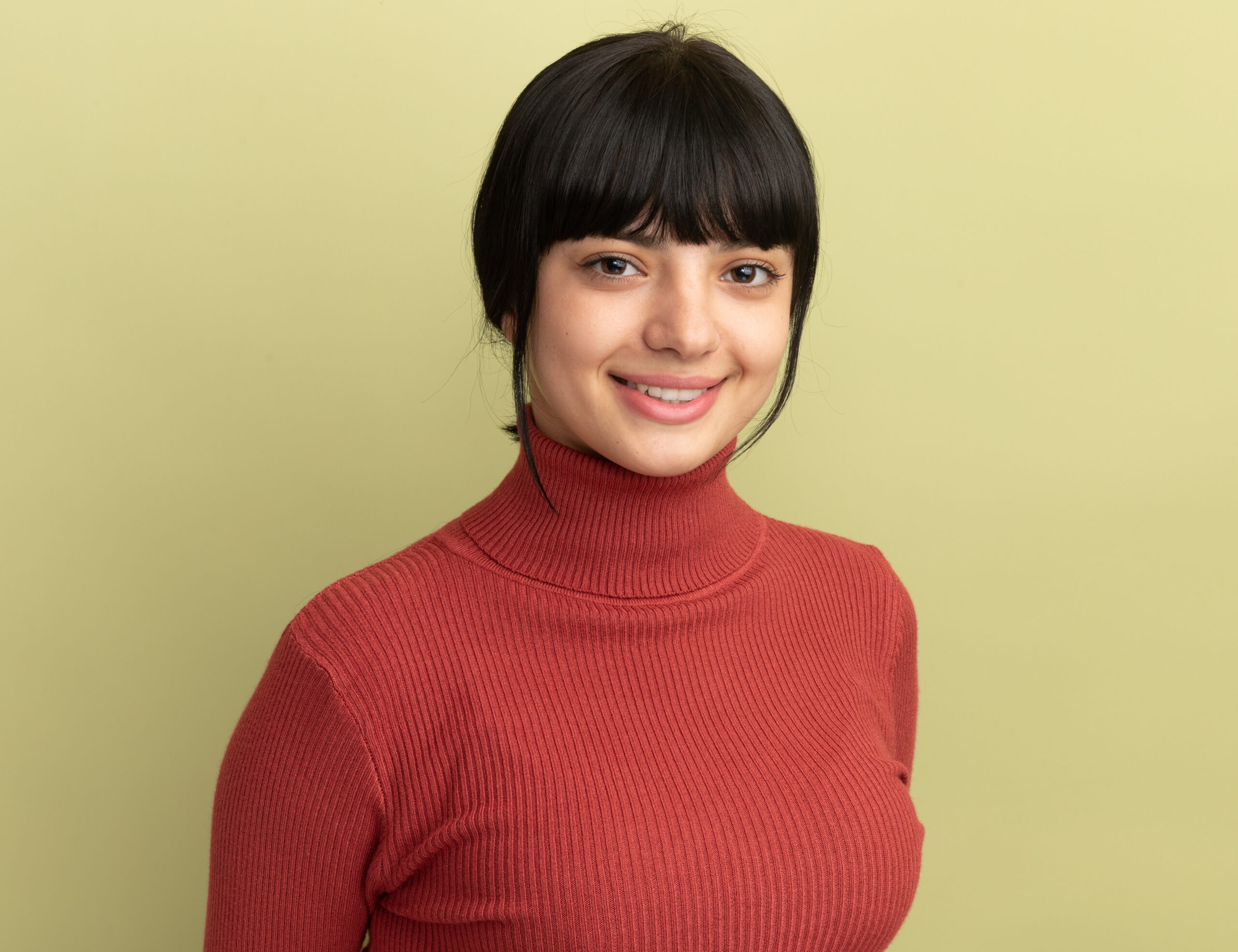 smiling young brunette caucasian girl looks at camera isolated on olive green background with copy space